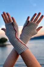 Load image into Gallery viewer, Photo advertising knitting pattern for fingerless mitts. Photo shows two hands extended in the air with a river in the backdrop. The mitts are made with grey alpaca and feature brioche stitches and a red seam.